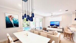A modern living room with a white sofa, dining table, and chairs. There is a TV on the wall and a painting of a mermaid. - Islamorada Florida Bay Villa  Plunge Pool, Boat Dock, Amazing Sunset Views (Islamorada)