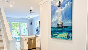 A modern kitchen with a wooden floor, white cabinetry, and a painting of a lighthouse on the wall. - Islamorada Florida Bay Villa  Plunge Pool, Boat Dock, Amazing Sunset Views (Islamorada)