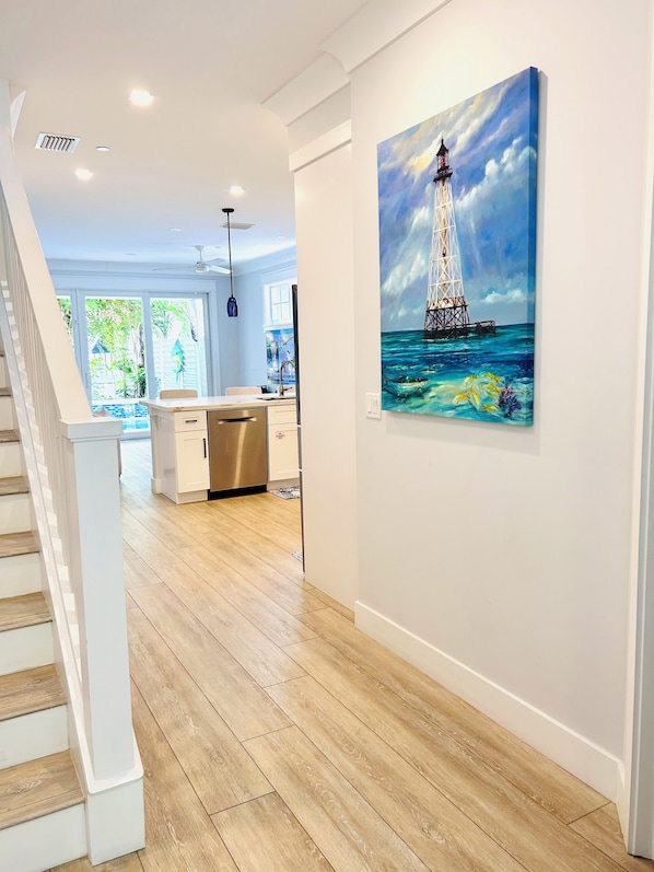 A modern kitchen with a wooden floor, white cabinetry, and a painting of a lighthouse on the wall.