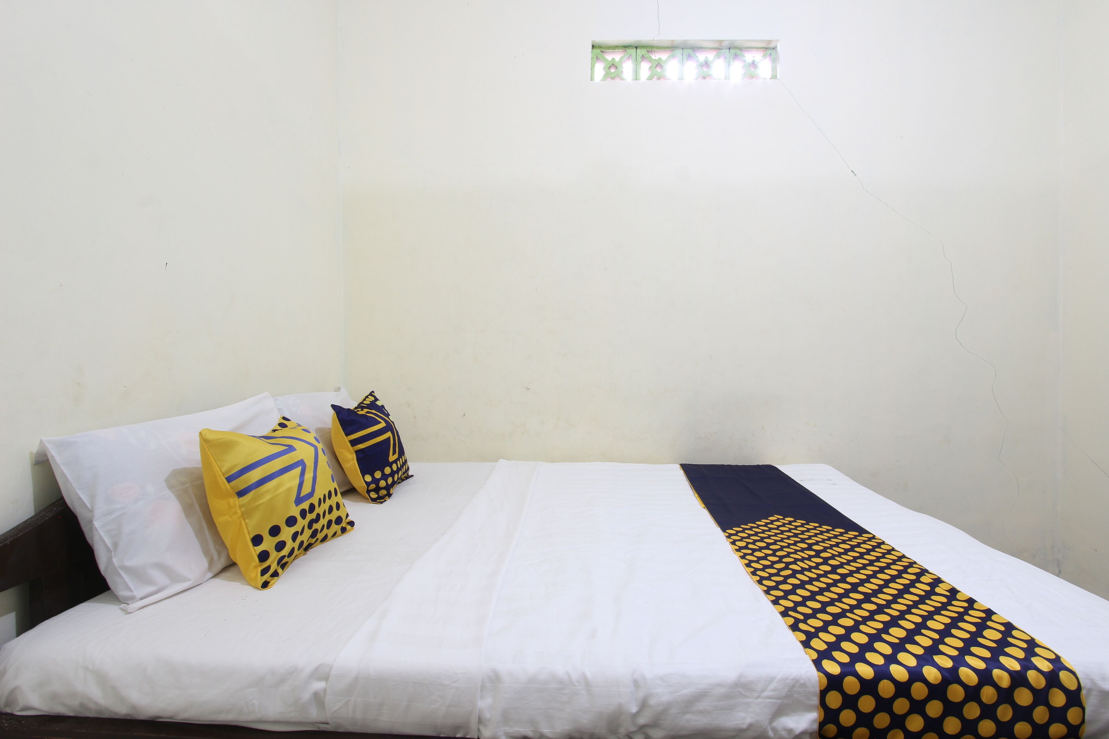 A single bed with white bedding and two decorative pillows, one with a geometric pattern and the other with a polka dot design.