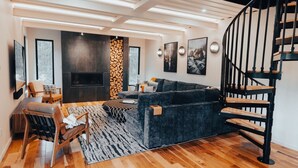 A modern living room with a dark blue sofa, wooden flooring, a black staircase, and a fireplace. - Pacific Bin - Sauna / Hot Tub / Steam Room (Monroe)