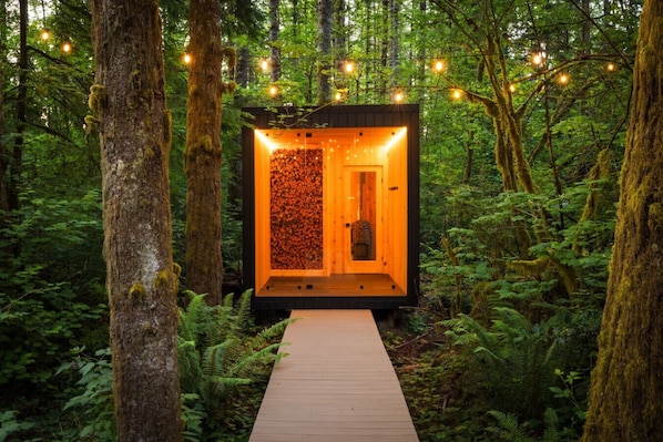 A wooden cabin with a wooden deck leading to it, surrounded by a forest.