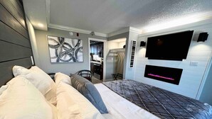 A hotel room with a bed, a flat-screen TV, and a wall-mounted fireplace.