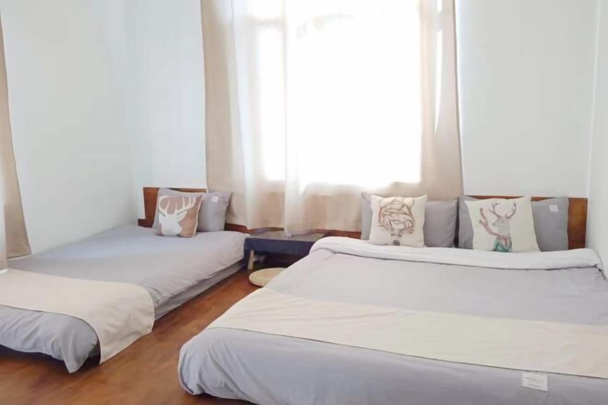 A room with two single beds, a small table, and a window with curtains.
