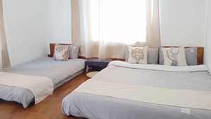 Una habitación con dos camas individuales, una mesita pequeña y un ventanal con cortinas.