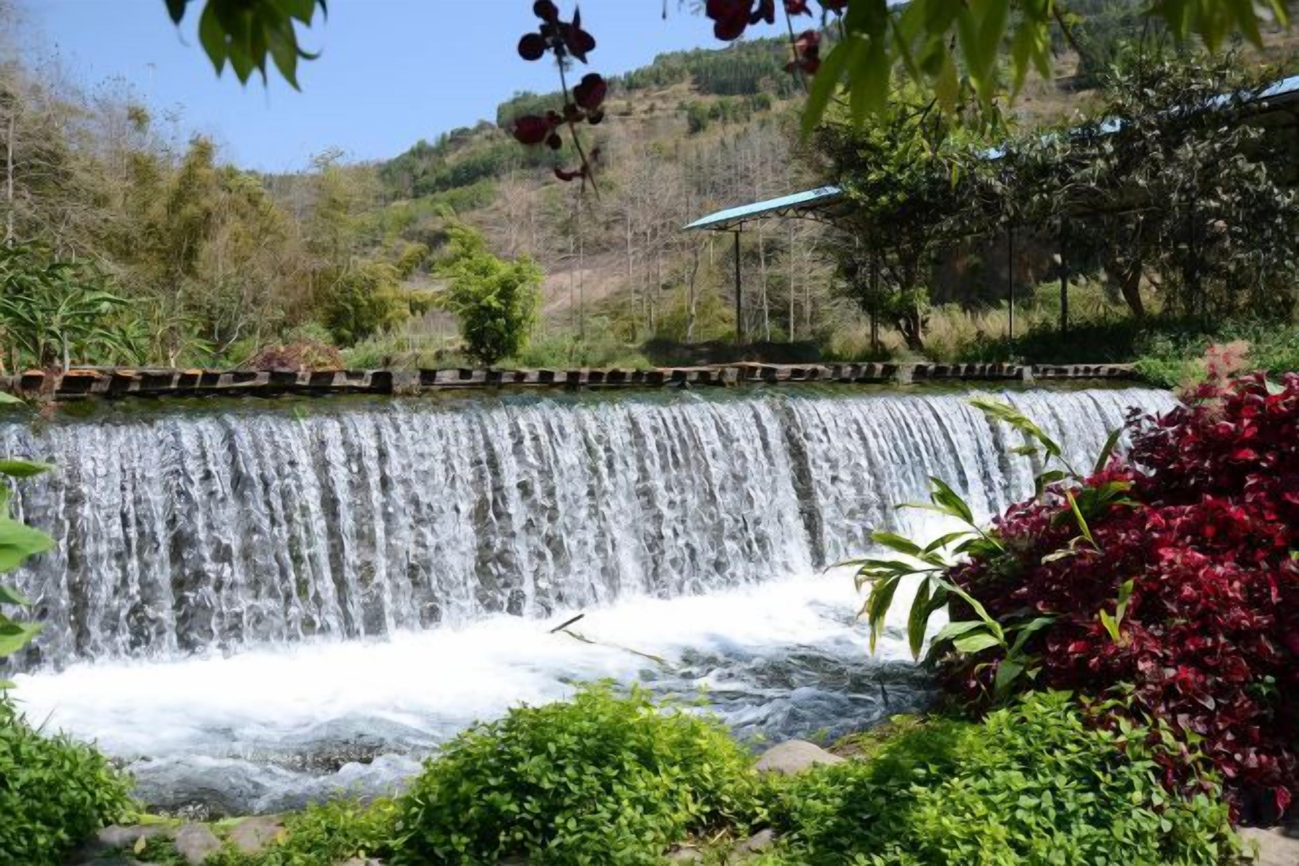A waterfall cascading over a man-made structure surrounded by lush greenery.