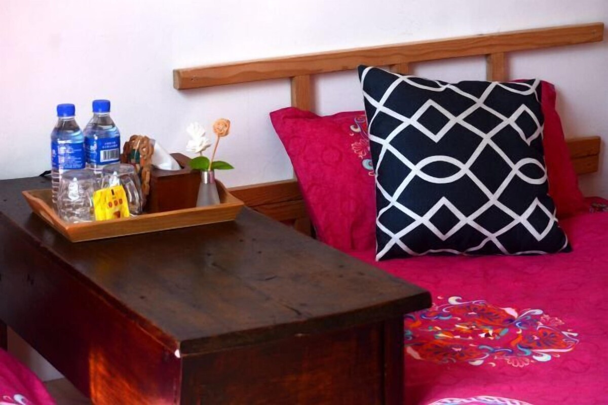 A bed with a wooden headboard, a black and white patterned pillow, a red pillow, and a floral bedspread.