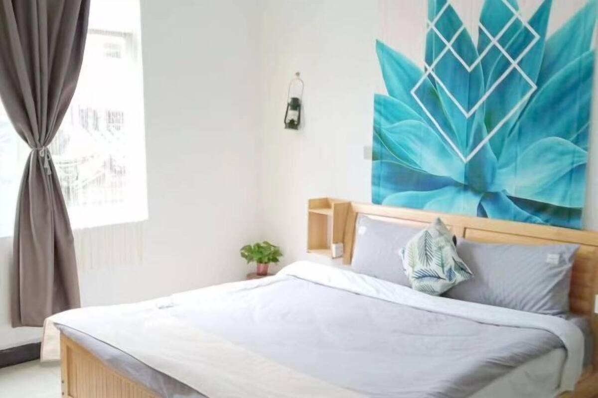 A bedroom with a bed, a wall-mounted heater, a window with curtains, and a wall art piece.