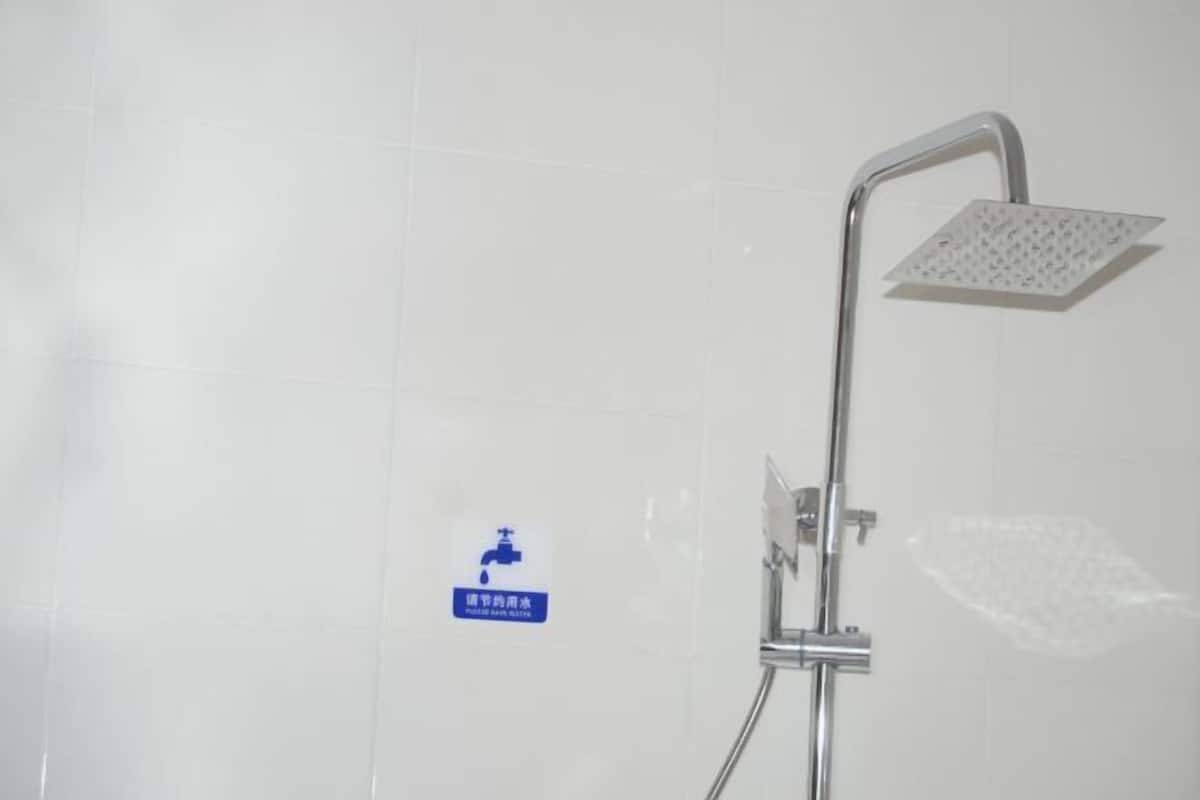 A shower with a square head and a handheld showerhead, a wall-mounted faucet, and a sign indicating water conservation.