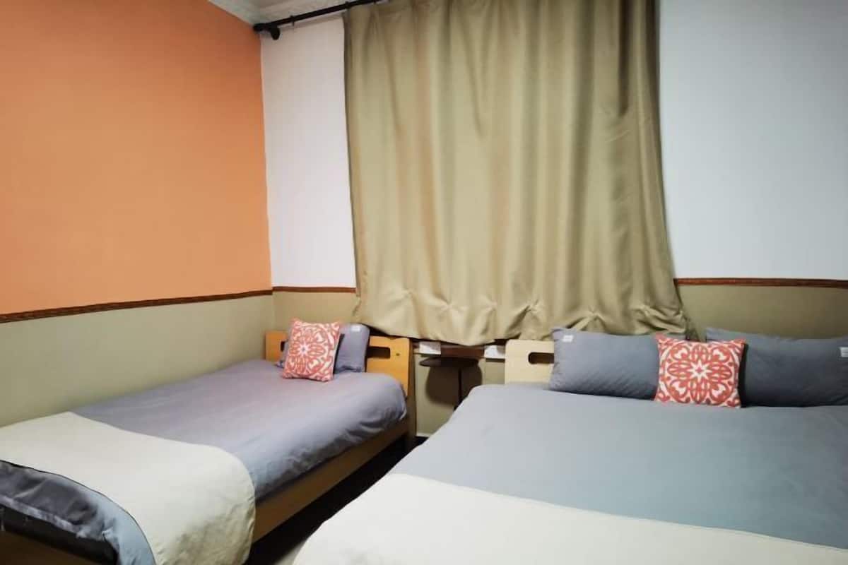 Two single beds with headboards, a window with beige curtains, and a wall with a brown trim.