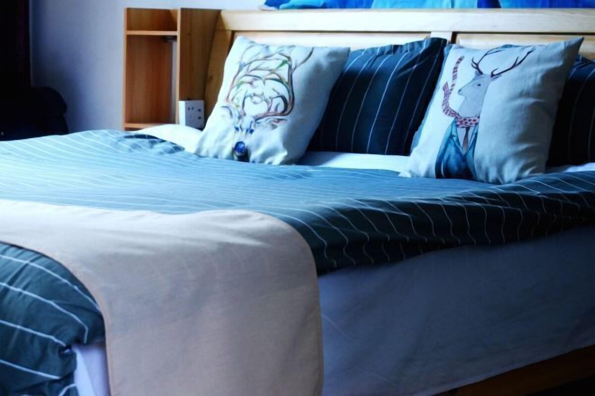 A neatly made bed with striped bedding and decorative pillows, a wooden headboard, and a bedside table with a lamp.