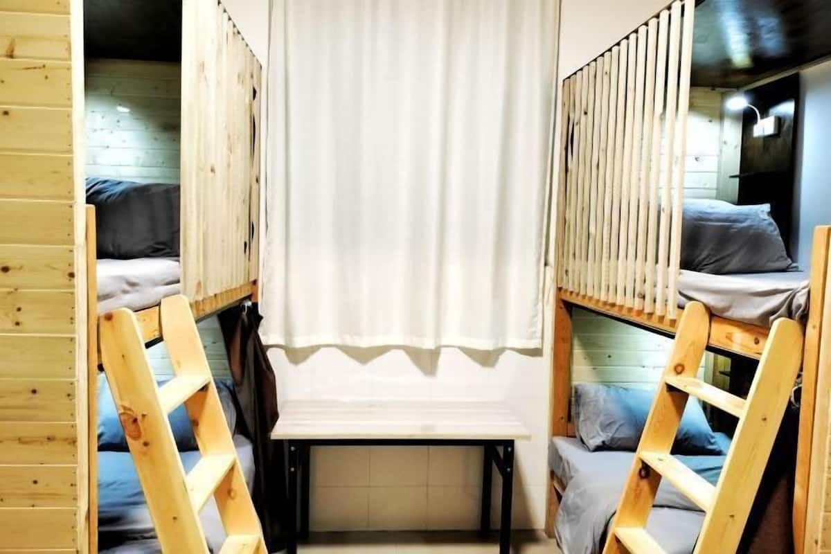 A dormitory room with bunk beds, a small table, and a curtain.