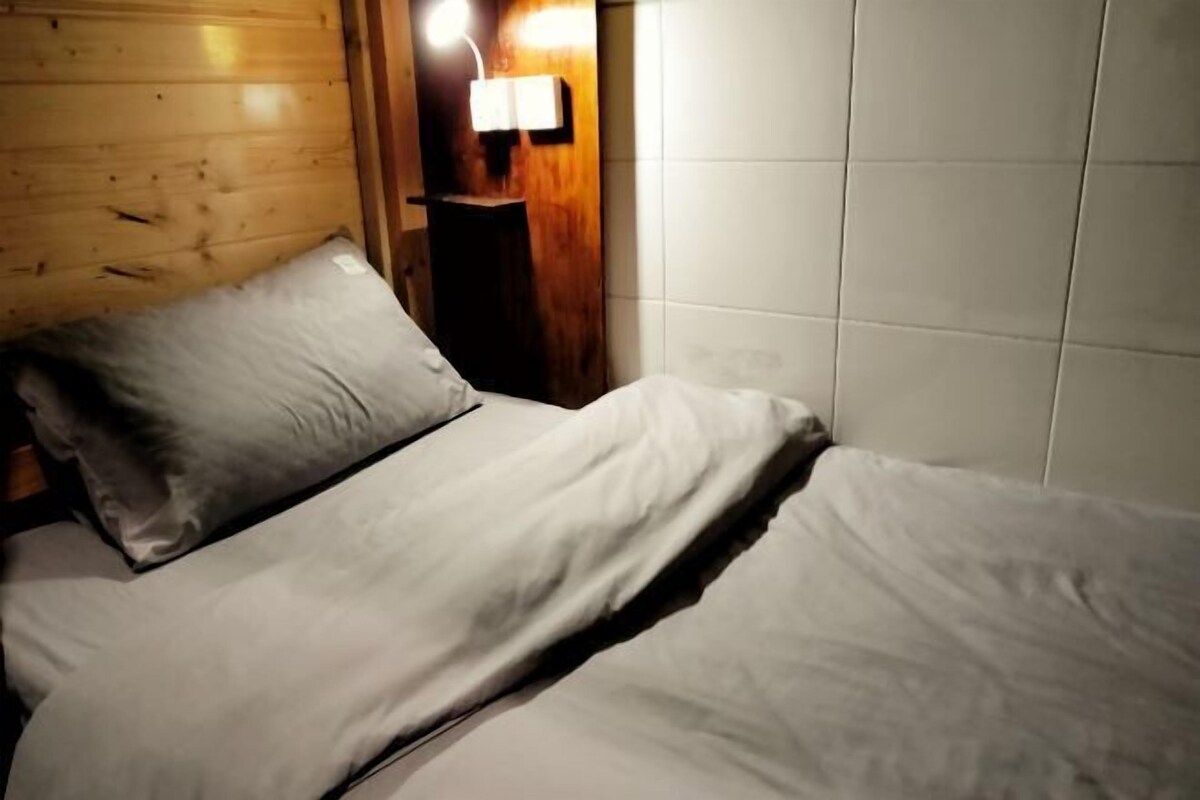 A bed with white linens in a room with wooden walls and a tiled wall.