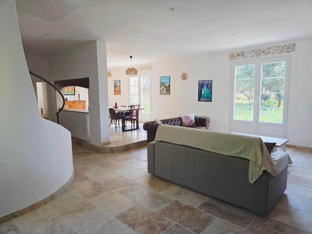 A spacious living area with a curved staircase, a sofa, and a dining area with chairs and a table.