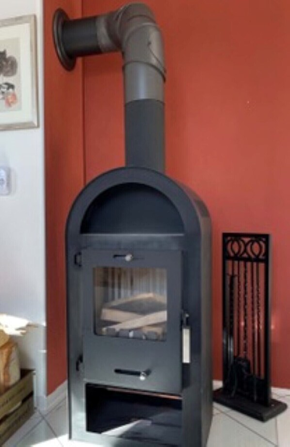 A wood-burning stove with a chimney, a window, and a metal grate. - Spacious, quiet, A/C , Espresso machine, 2 queen beds, 50” Netflix TV, (Aarbergen)