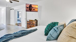 Une chambre avec un lit, un ventilateur de plafond, un téléviseur fixé au mur et une vue sur l’extérieur.