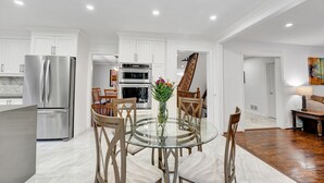 Une cuisine moderne avec des meubles blancs, des appareils en acier inoxydable et un coin repas comprenant une table en verre et des chaises en bois.