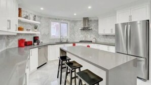 Une cuisine moderne avec des meubles blancs, un réfrigérateur en acier inoxydable et un îlot central doté de tabourets de bar.