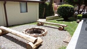 An outdoor seating area with a fire pit, wooden benches, and a small building with a window. - A Nossa Casinha (Campos do Jordão)