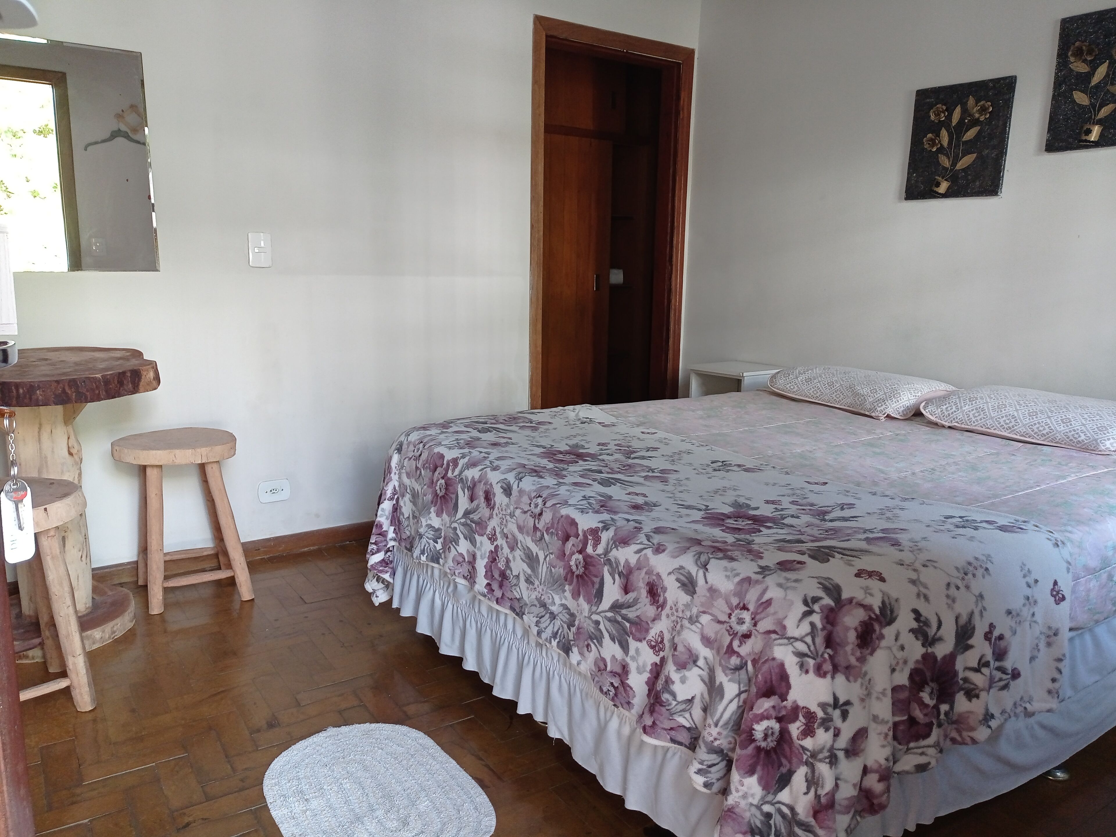 A bedroom with a floral bedspread, a wooden stool, a small round table, and a white rug.