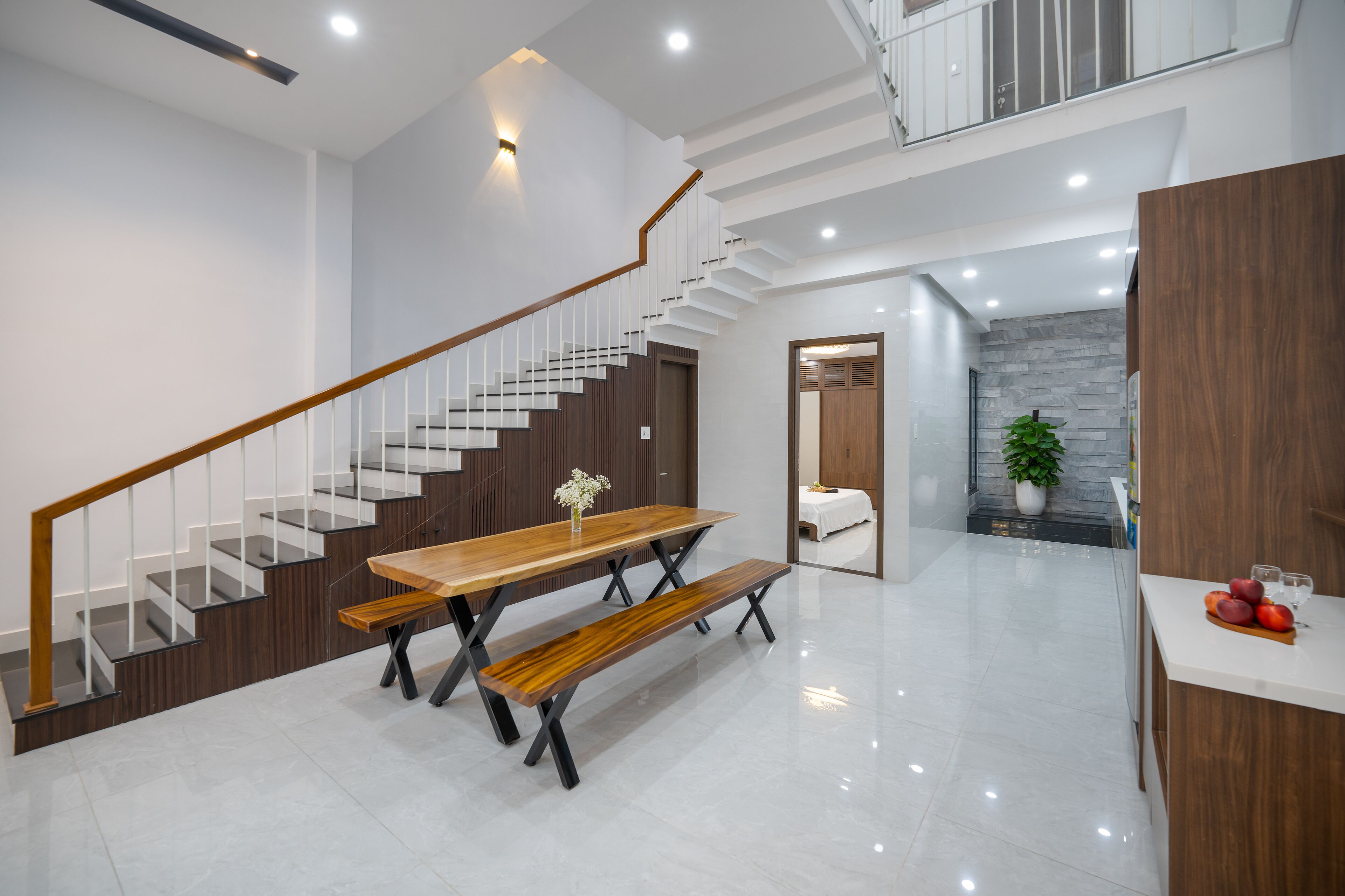 A modern kitchen with a wooden table and bench, a staircase, and a potted plant.