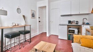 A compact kitchen with white cabinets, a microwave, and a sink. There is a small dining area with two stools and a table.