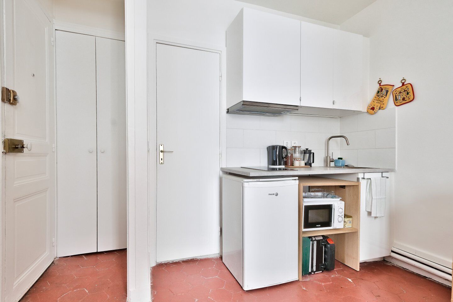 A compact kitchen with white cabinets, a small refrigerator, a microwave, and a sink.