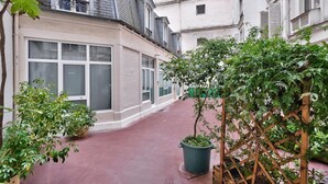 A narrow alleyway with a building featuring large windows and a red pavement.