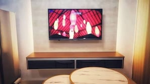 A TV mounted on a wall above a wooden bench with two round tables in front. - Serenity Cove MOA Cozy condo unit amenity view. (Pasay)