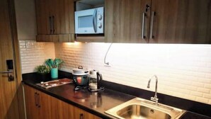 A modern kitchen with wooden cabinets, a stainless steel sink, a microwave, and a coffee maker. - Serenity Cove MOA Cozy condo unit amenity view. (Pasay)