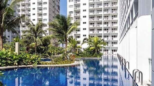 A modern hotel with a pool surrounded by lush greenery and tall buildings in the background. - Serenity Cove MOA Cozy condo unit amenity view. (Pasay)
