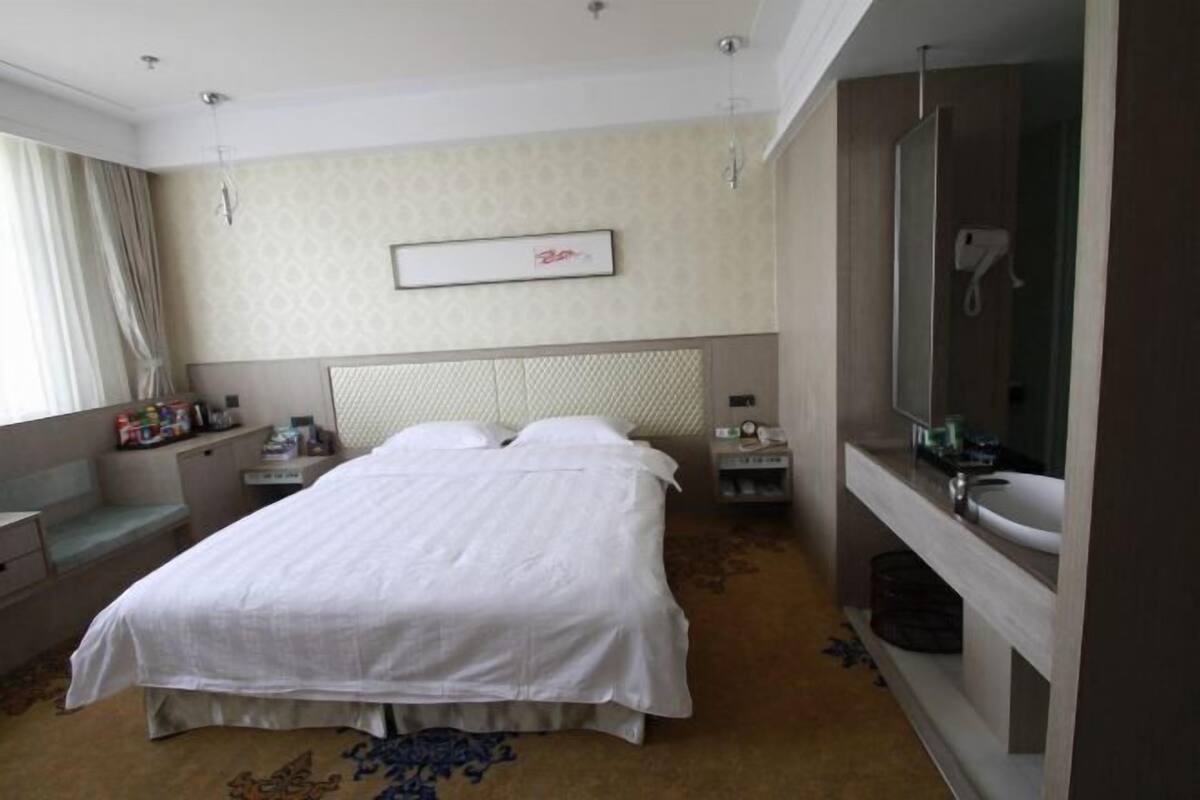 Una habitación de hotel con cama, mesitas de noche, espejo y ventana con cortinas.
