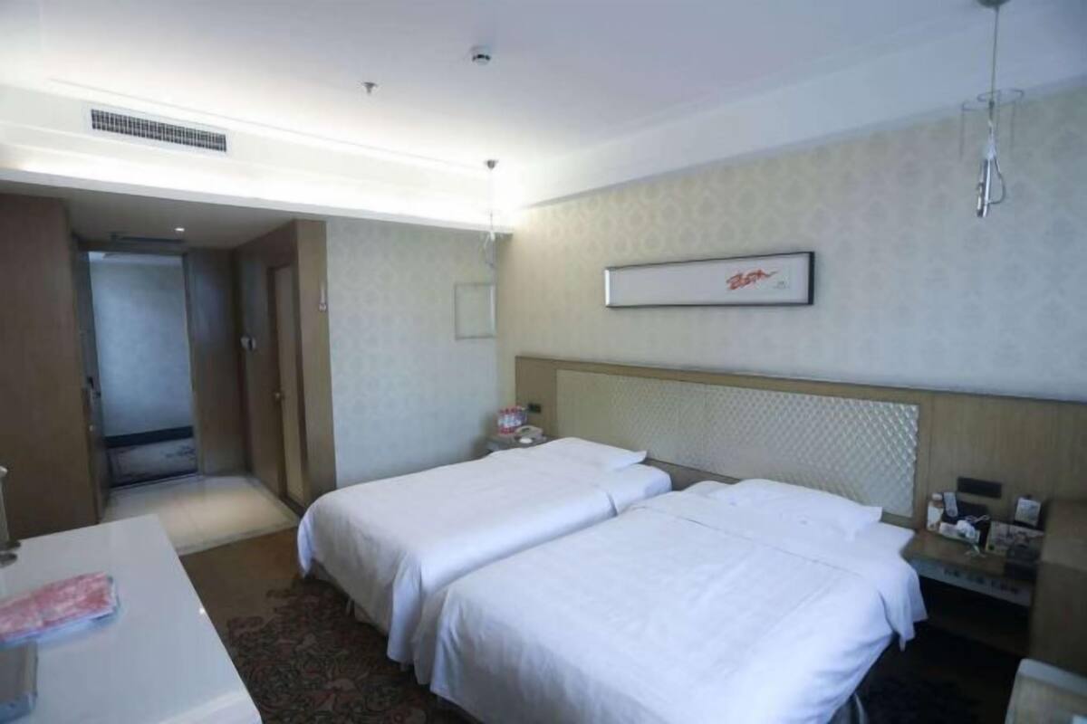 Habitación de hotel con dos camas individuales, un escritorio con silla, una mesita de noche, un espejo y una puerta que da a un baño.