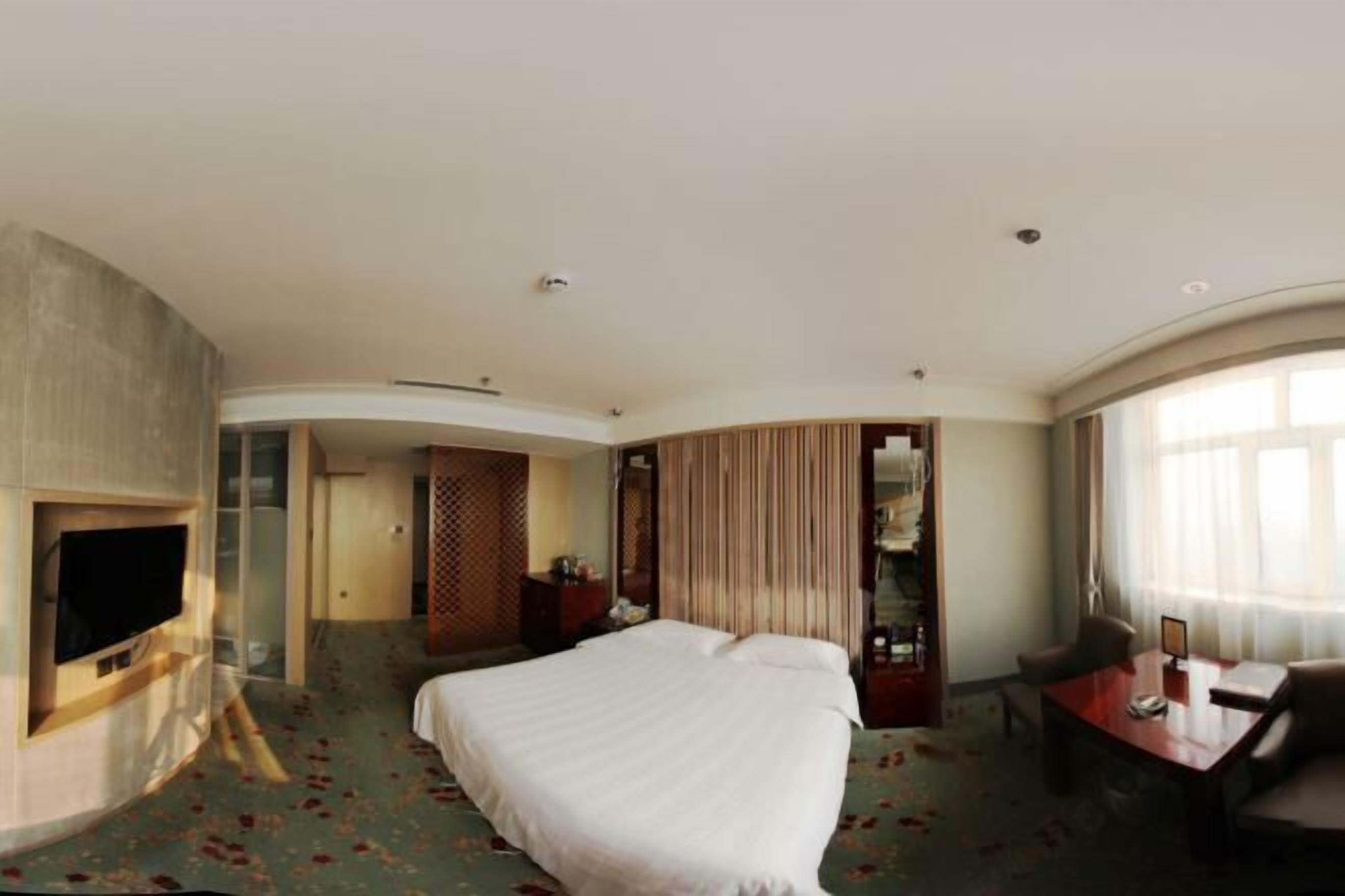 Una habitación de hotel con cama, escritorio, televisor y un amplio ventanal.