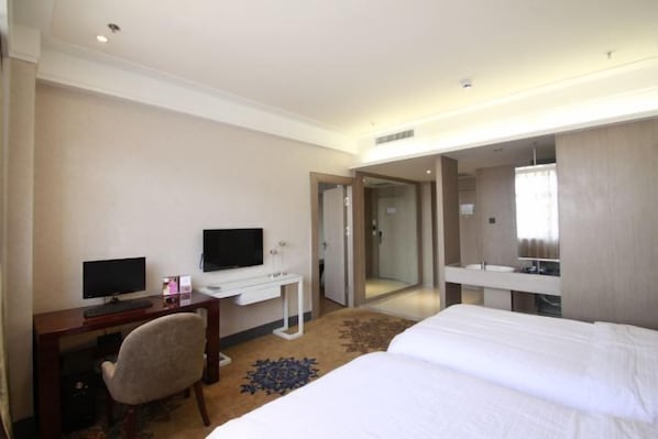 A hotel room with a bed, a desk with a computer, a chair, a TV, and a bathroom with a mirror and sink. - Linton Hotel (Huanan)
