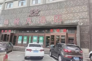 A hotel with a brick facade, multiple entry doors, and several cars parked in front. - Linton Hotel (Huanan)