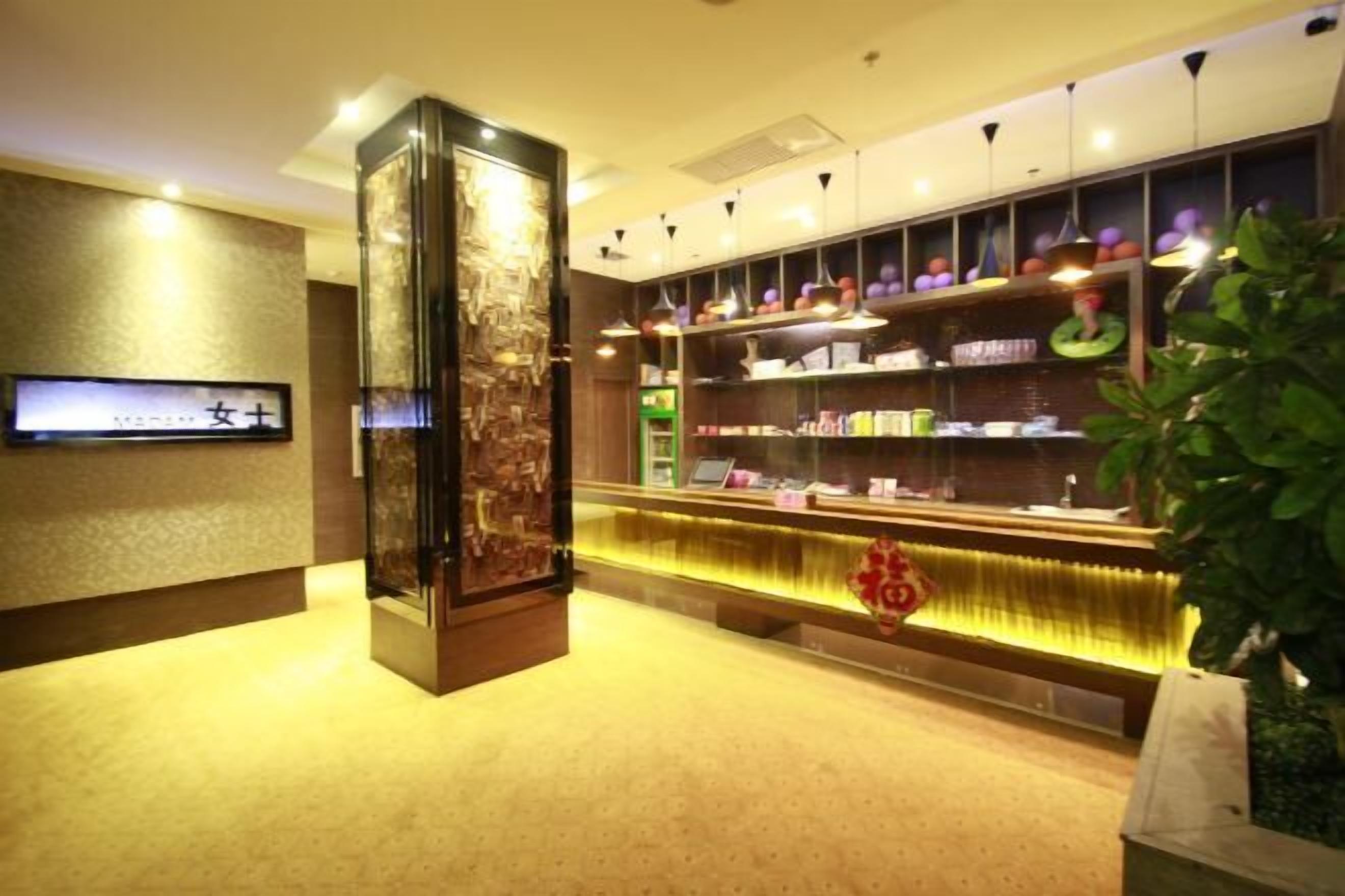 Un espace d’accueil d’hôtel au design moderne, comprenant un comptoir d’accueil, des étagères remplies de produits et une grande colonne décorative.