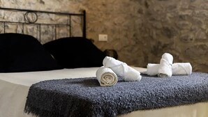 A bed with a dark blue blanket, two rolled white towels, and a stone wall in the background. - Mas Ribas Turismo Rural (Ventallo)