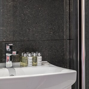 A bathroom with a white sink, a mirror, and a dark speckled wall. - Designer 1-bedroom in Kensington (London)