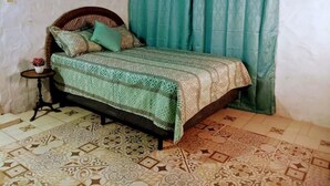 Un dormitorio con una colcha estampada, una mesita de noche con una planta y una cortina.