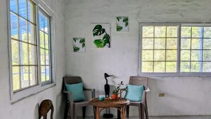 Habitación con dos sillas, una mesita pequeña y una planta en maceta. Se ven dos ventanas con vistas a la vegetación.
