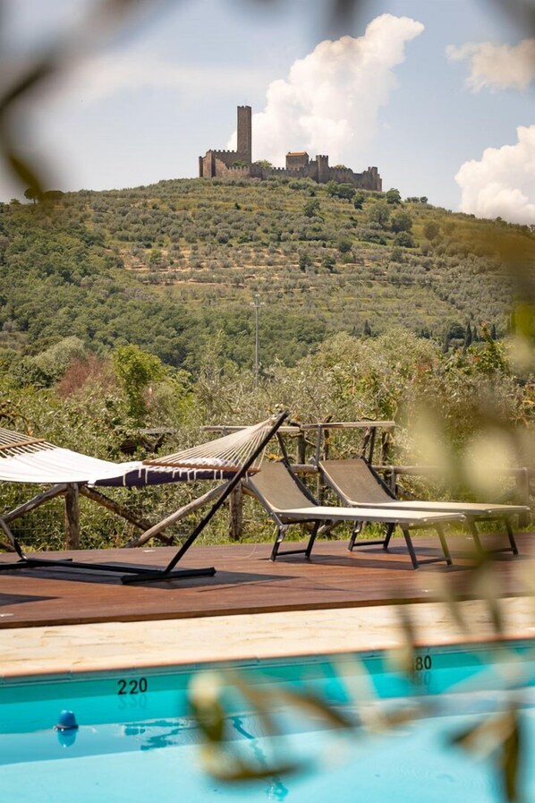 A pool area with lounge chairs and a view of a castle on a hill.