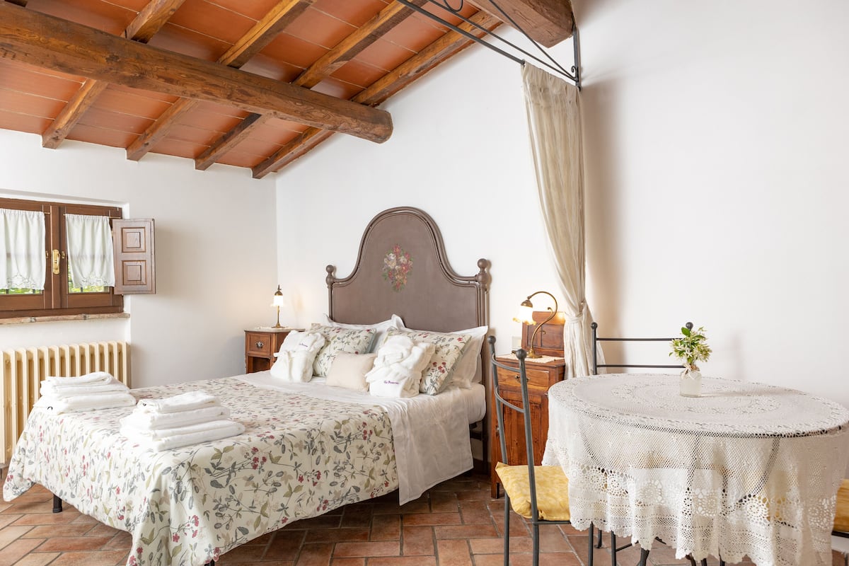 Ein Schlafzimmer mit einem Doppelbett, einem runden Tisch mit Spitze und einer Holzbalkendecke.