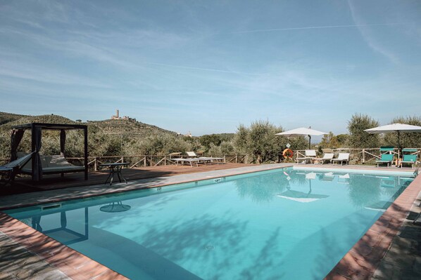 A swimming pool with lounge chairs and umbrellas, surrounded by a wooden deck and greenery.