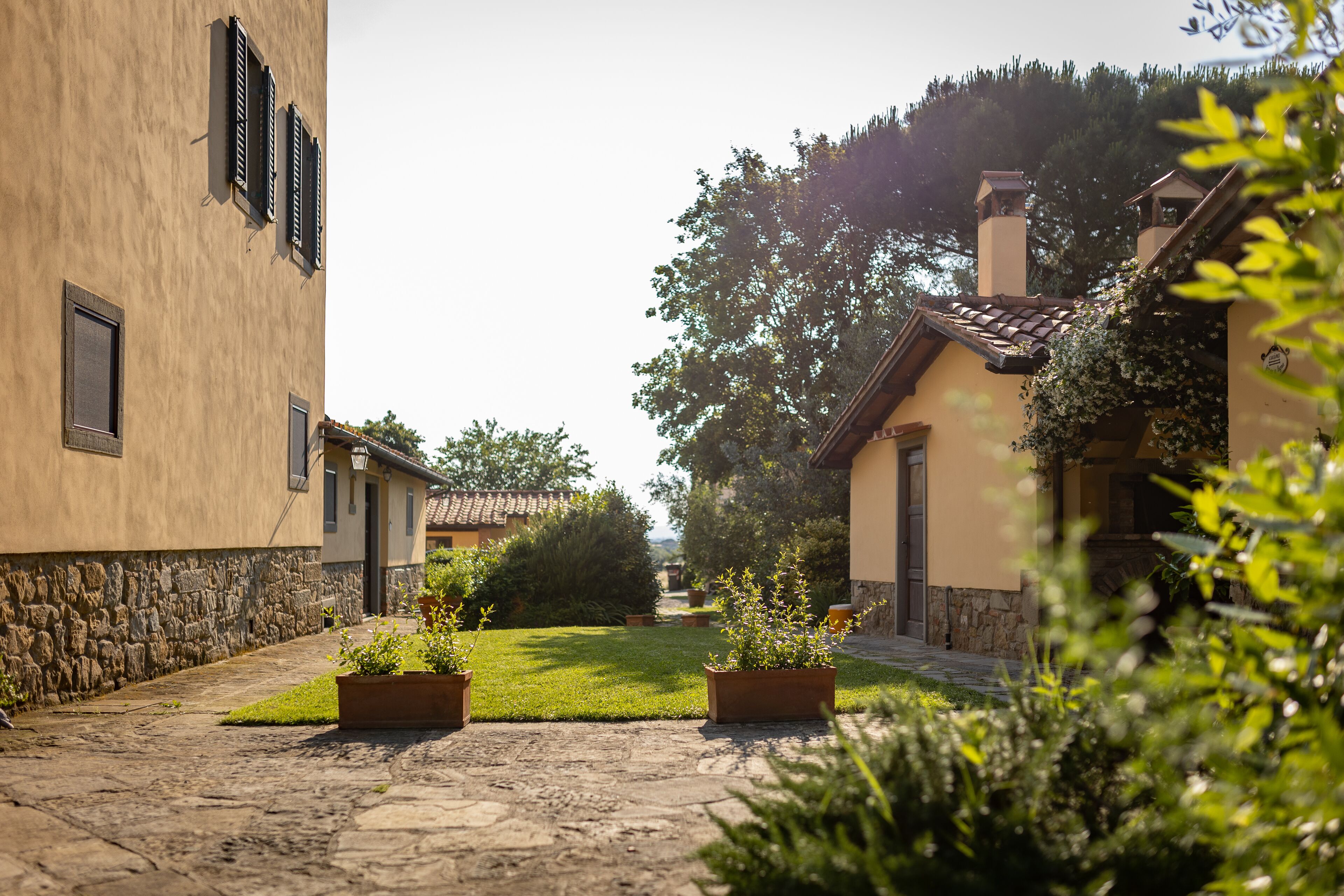 Un patio con pavimento de piedra, plantas en macetas y edificios con muros de piedra y techos de tejas.