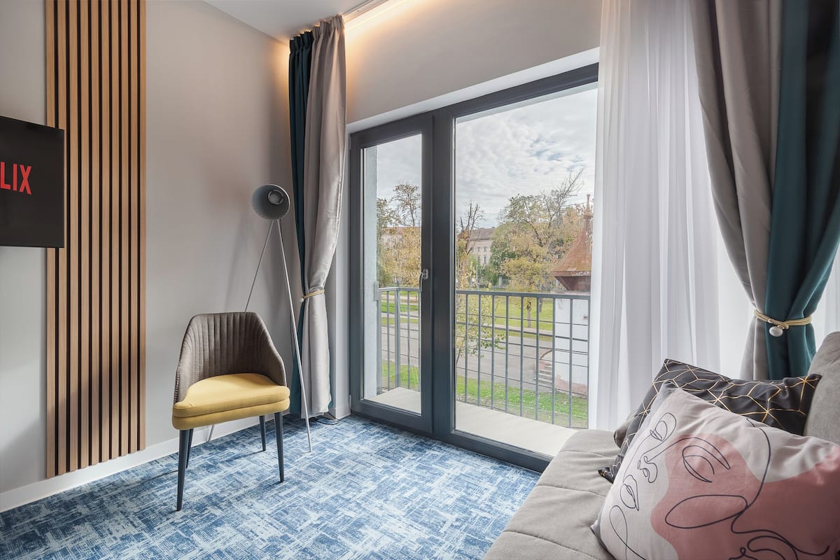 A modern room with a large sliding glass door to the outside, a chair, a sofa with decorative pillows, and a wall-mounted TV.