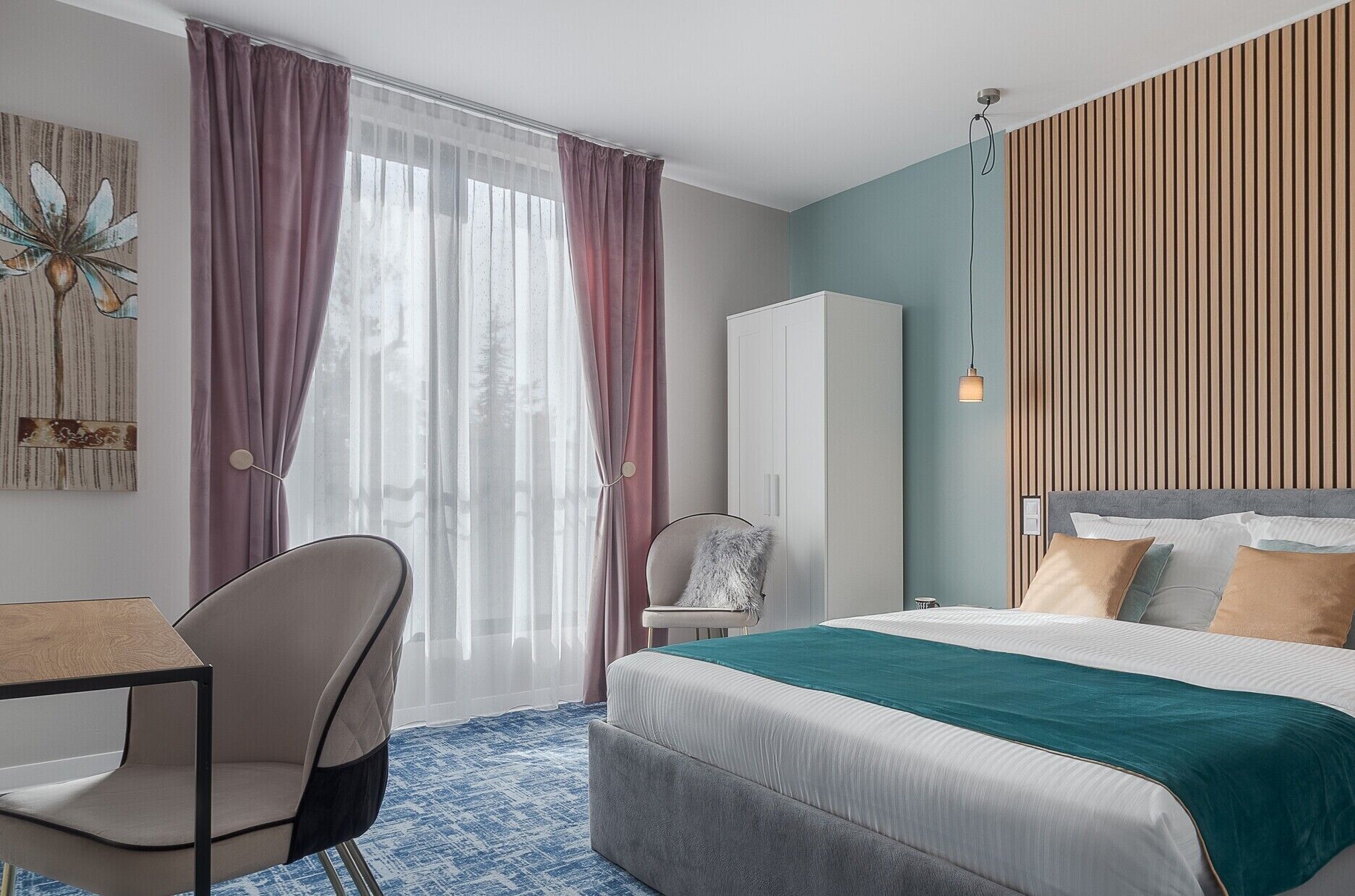 A modern hotel room with a bed, a desk, a chair, and a wardrobe.