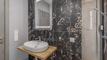 A modern bathroom with a marble backsplash, a wooden vanity, a round sink, a mirror, and a shower area.