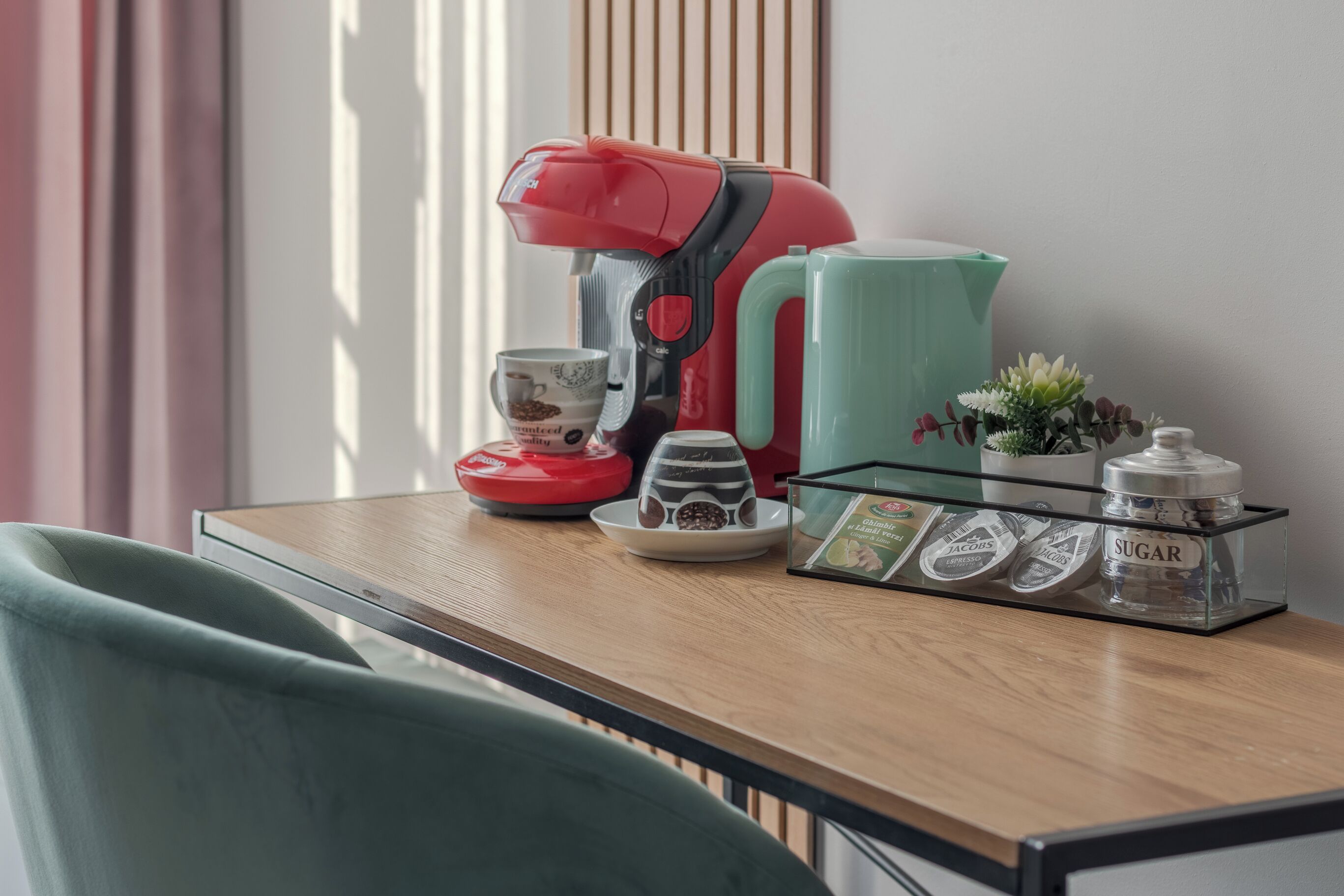 A kitchen counter with a coffee maker, a kettle, a sugar container, and a small potted plant.