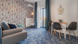 Ein modernes Wohnzimmer mit Wandmuster, einer Couch, einem Essbereich mit zwei Stühlen und Blick durch eine Glastür.